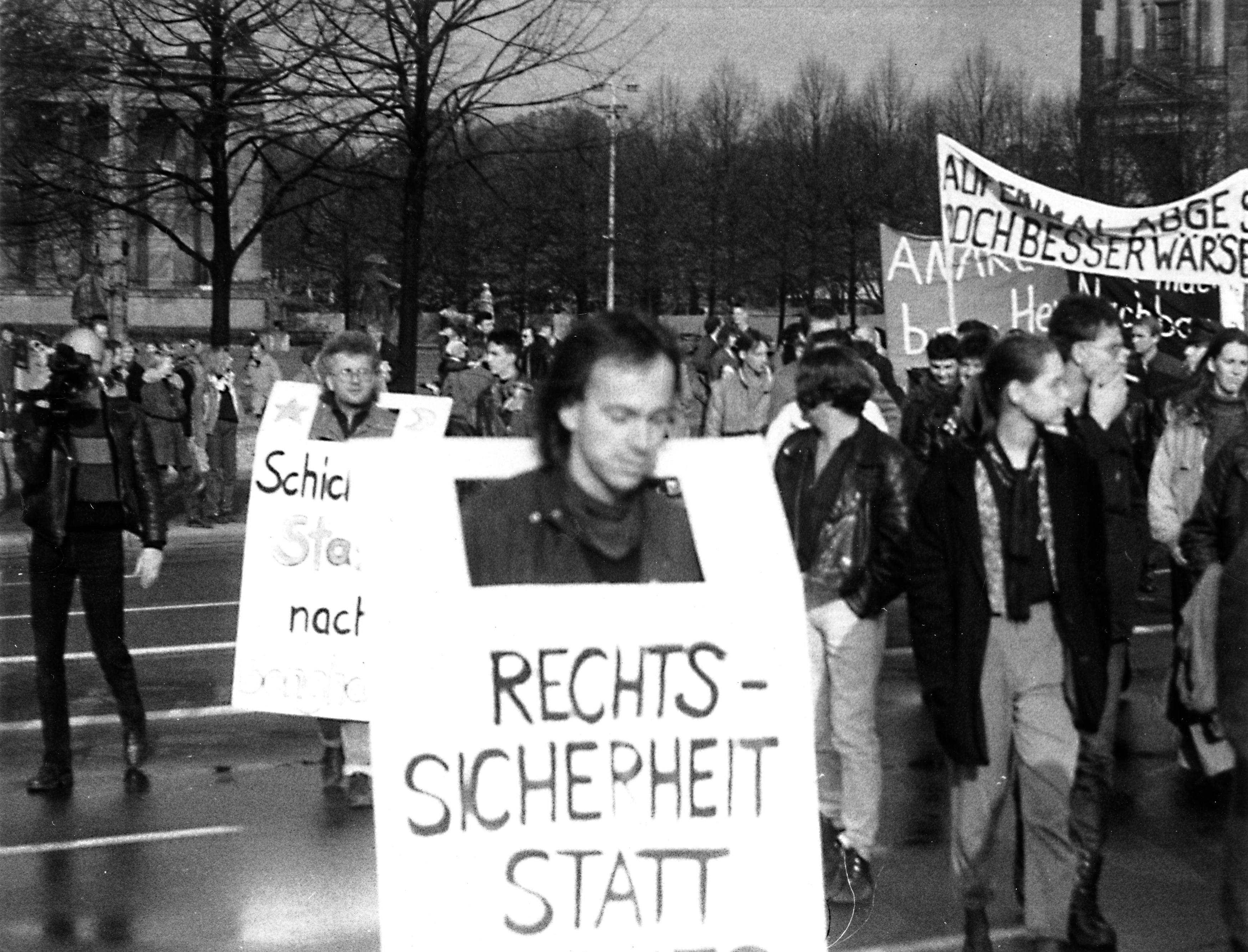 Demonstranten mit Transparenten und Plakaten. Vorne im Bild trägt ein Mann ein Transparent, worauf der Anfang des Schriftzuges "Rechtssicherheit statt" lesbar ist.