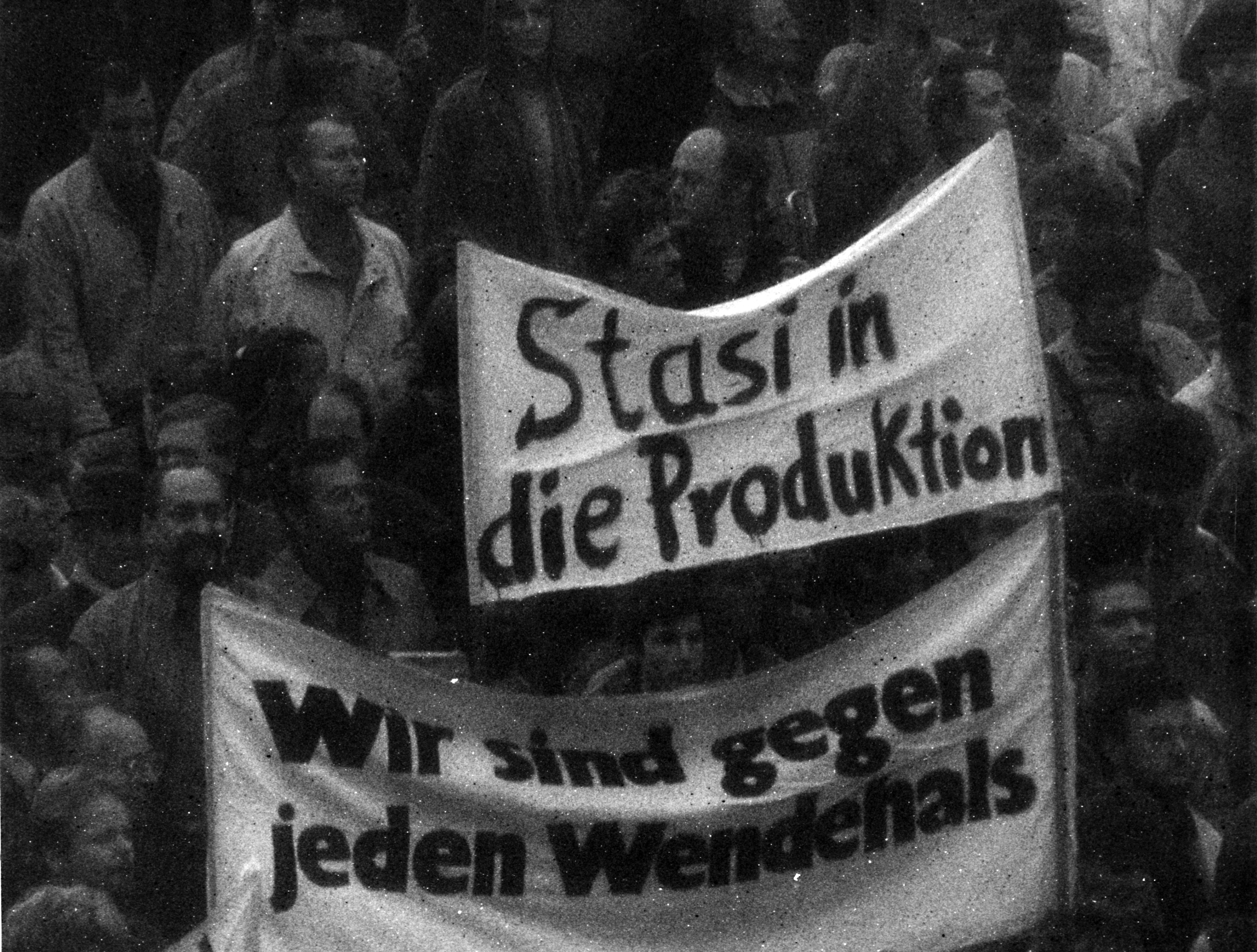 Blick auf Demonstration: Im Mittelpunkt des Bildes stehen zwei Transparente. Auf einem Transparent steht "Stasi in die Produktion", auf dem anderen "Wir sind gegen jeden Wendehals".